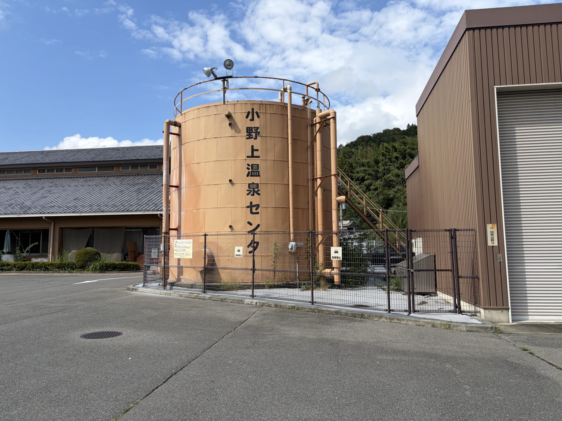 駐車場脇の橙色の大型タンク。側面に縦書きで「小野上温泉センター」