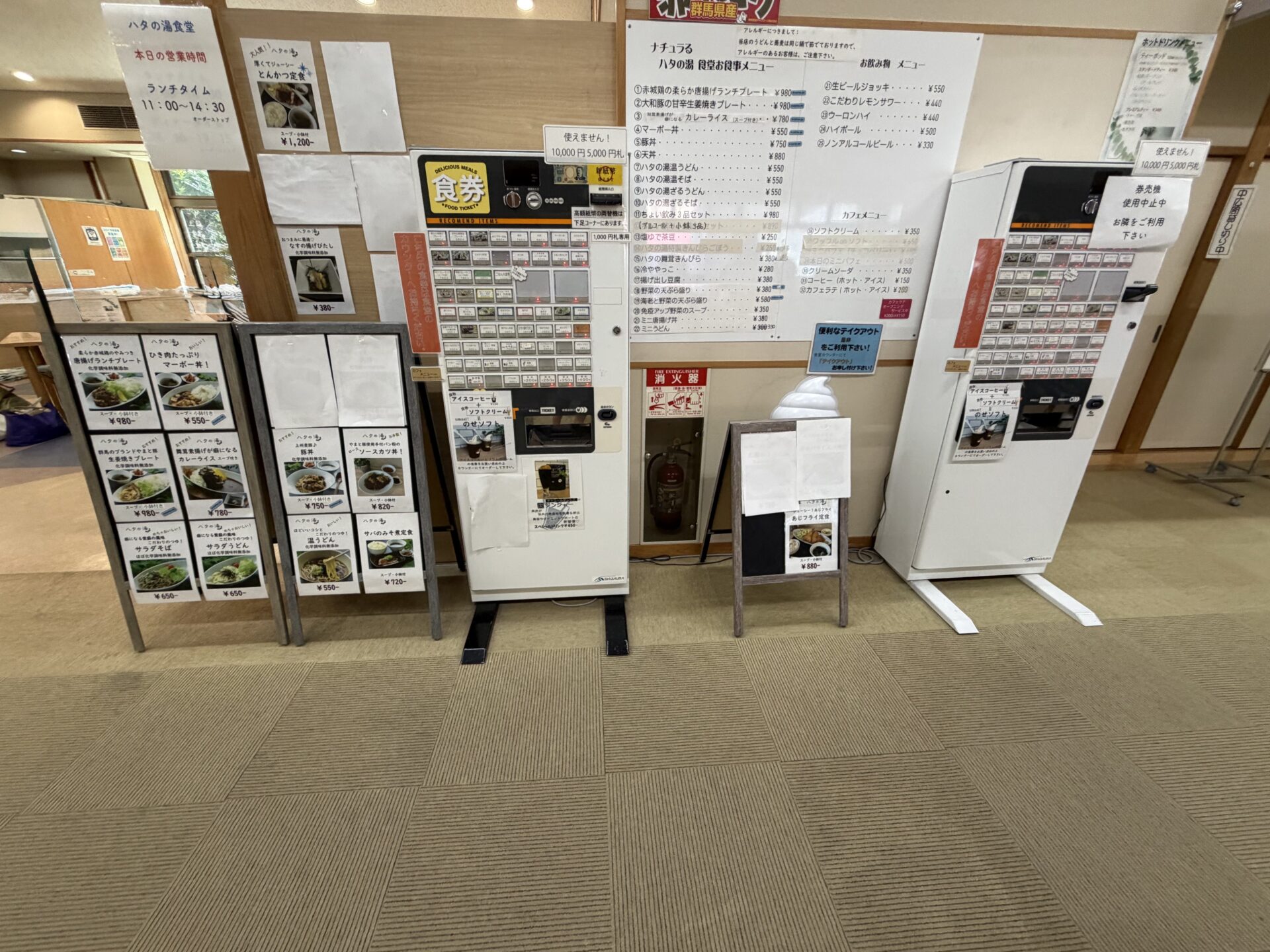 食堂前の券売機と壁一面の手書きメニュー。左上に「ハタの湯食堂 本日の営業時間 ランチタイム 11:00〜14:30」の掲示