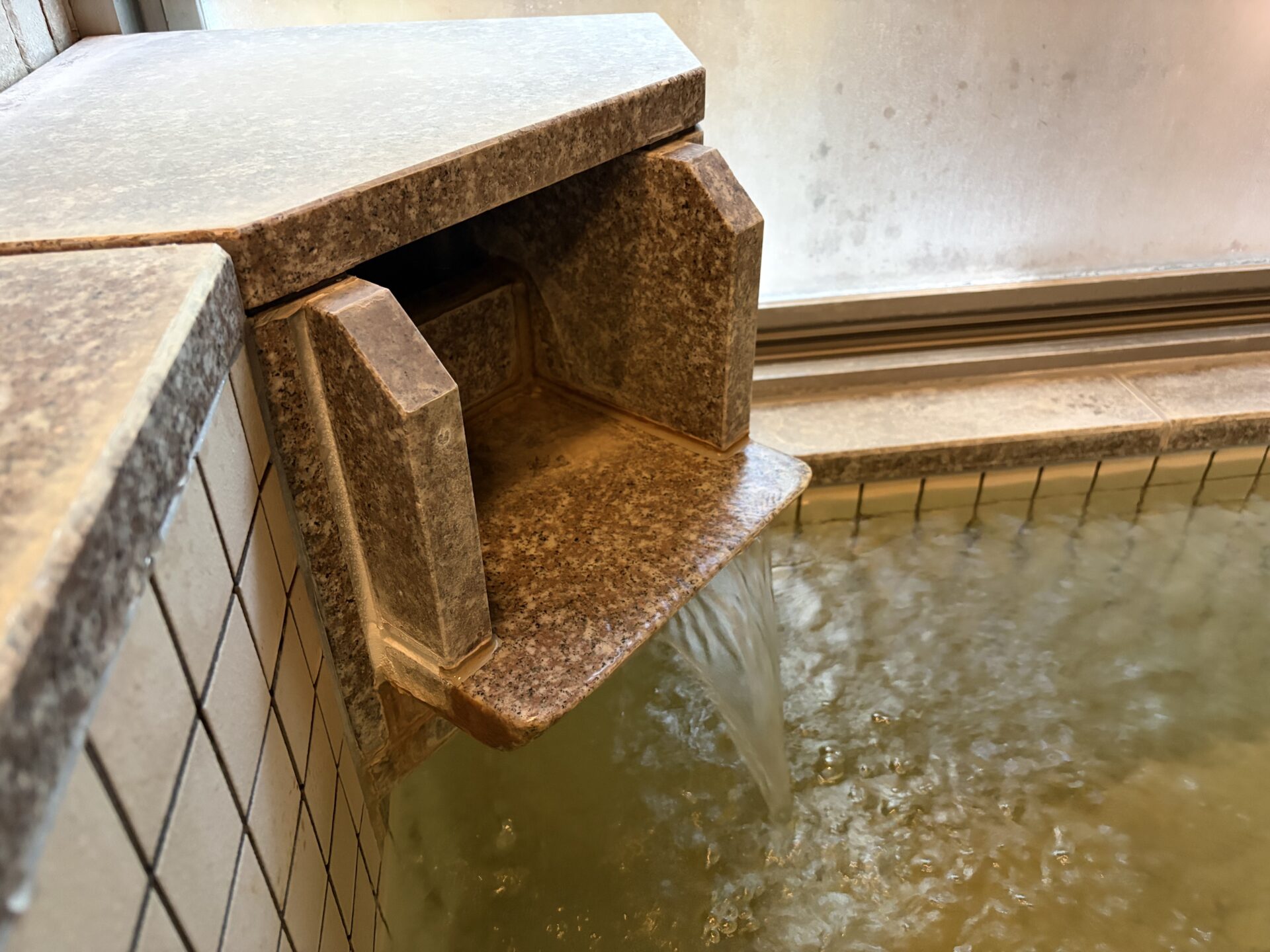 石を組んだ箱型の湯口。内側と縁が茶色い被膜に覆われ、湯が注がれている