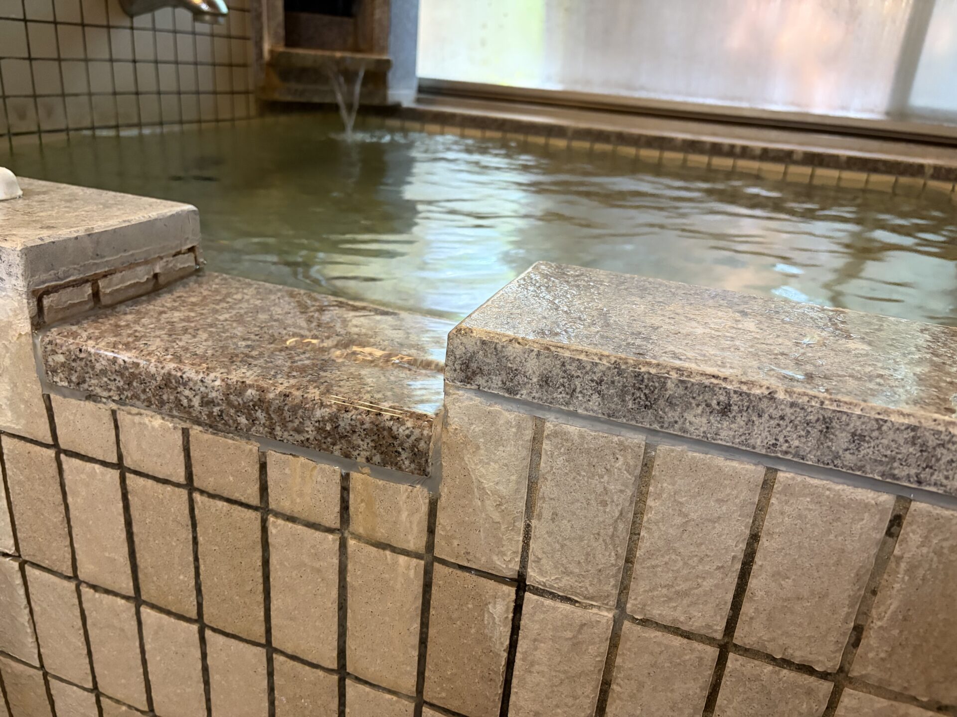 浴槽の縁。石の天端全面に湯が薄く流れ出している