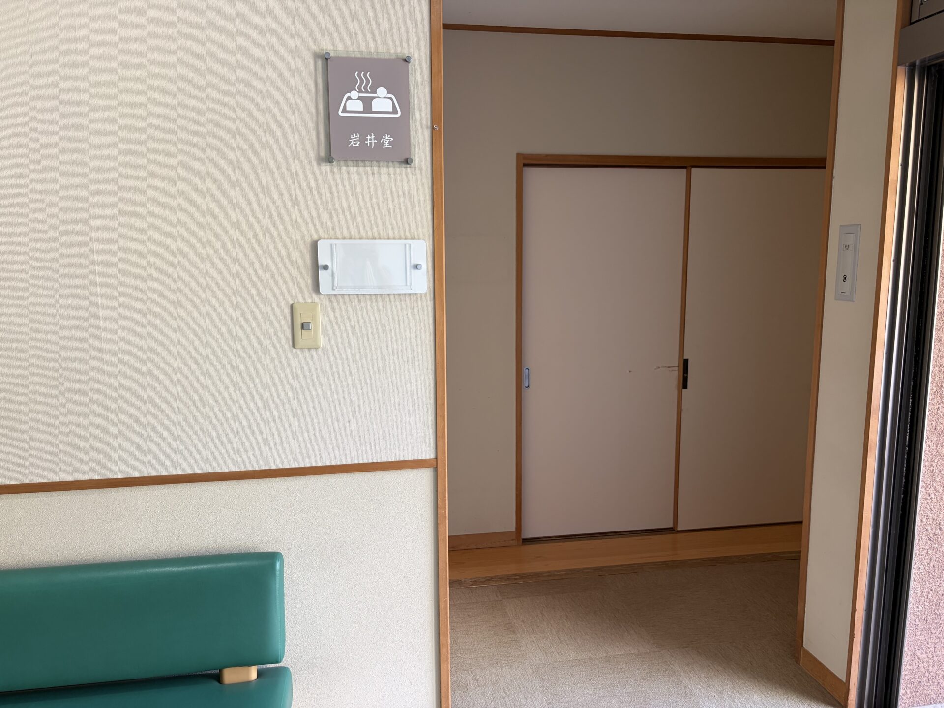 個室入口。茶系の室名札「岩井堂」と湯船のピクトグラム、手前に緑のベンチ