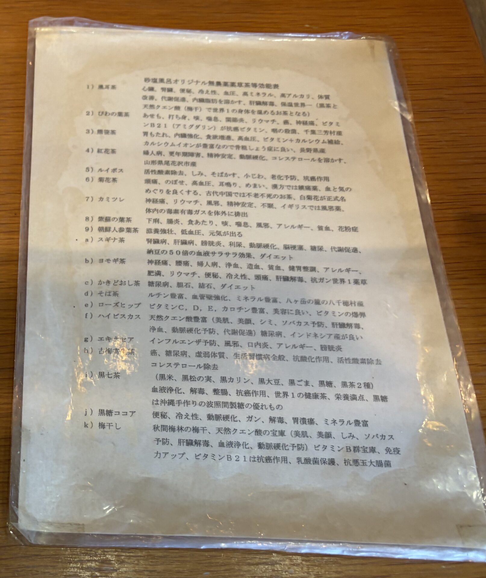 休憩コーナーの薬草茶一覧「砂塩風呂オリジナル無農薬薬草茶等効能表」。風耳茶から梅干しまで並ぶ