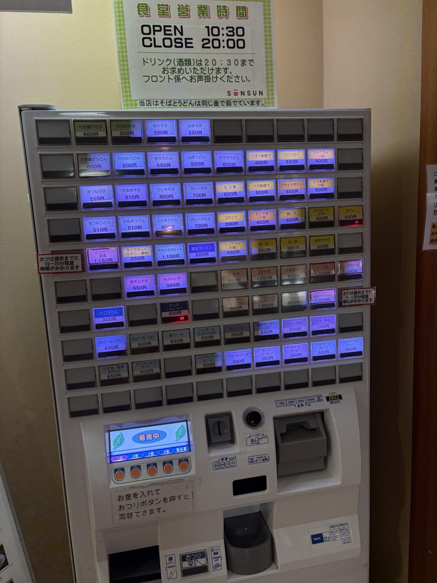食堂SUNSUNの券売機と営業時間の掲示。10:30〜20:00、酒類は20:30まで。「そばとうどんは同じ釜で茹でています」