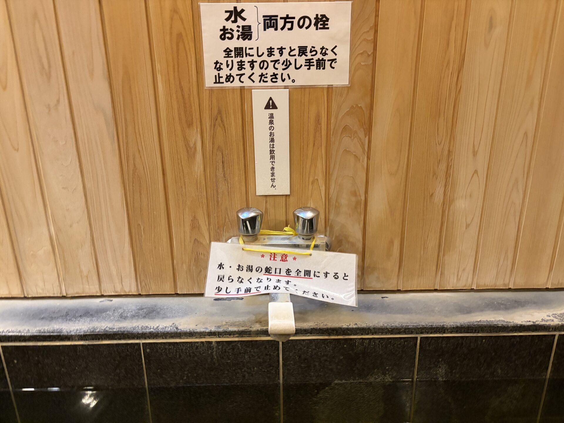 家族風呂の蛇口と張り紙。「全開にすると戻らなくなる」の注意が2枚と、「温泉のお湯は飲用できません」の札