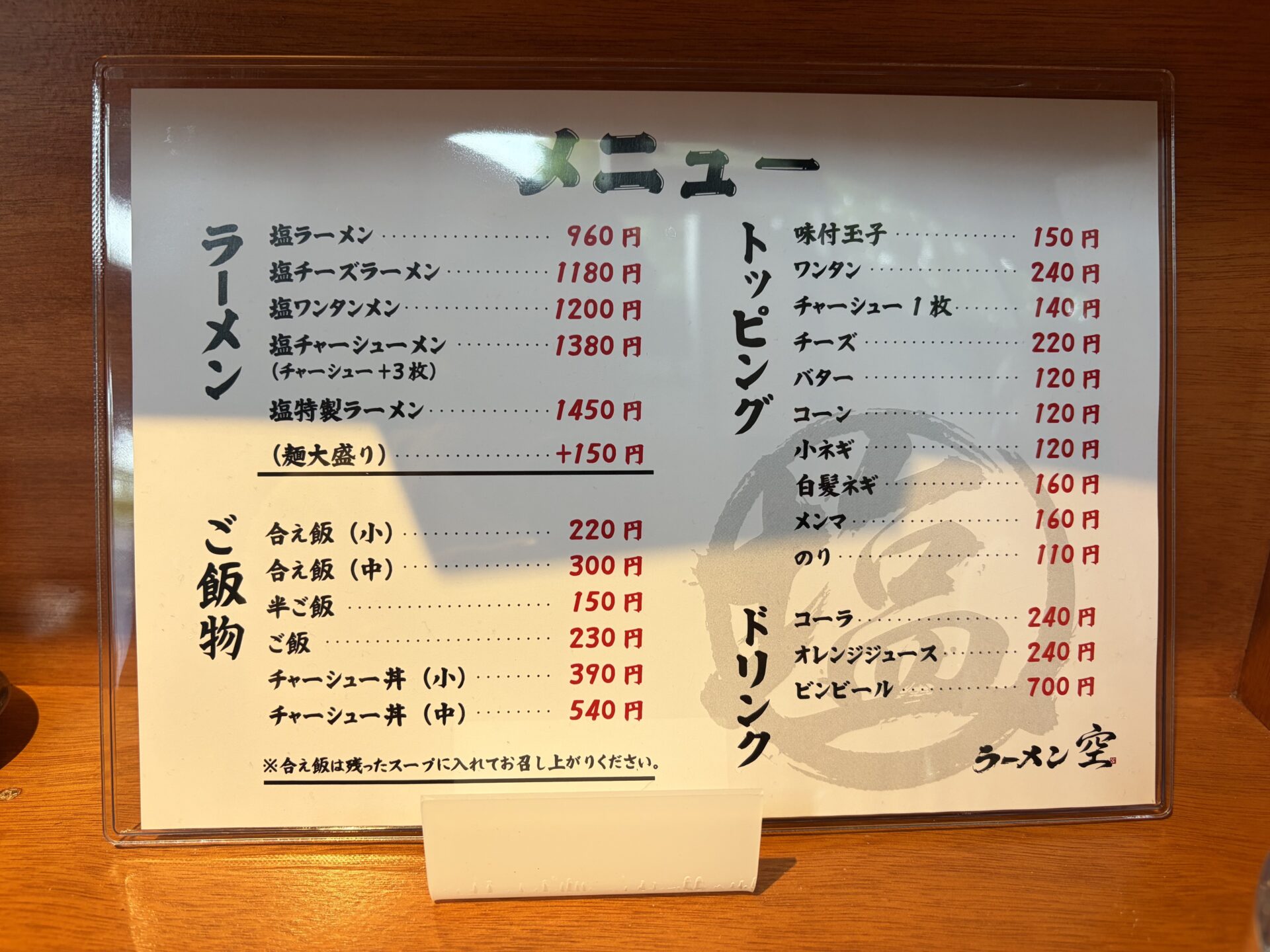 卓上のメニュー。ラーメン5種・ご飯物・トッピング・ドリンク。背景に大きな「塩」の筆文字