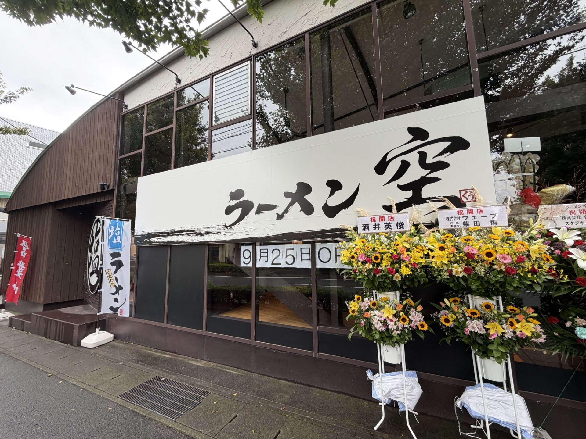 ラーメン空の外観。大きな筆文字の看板と、窓の「9月25日OPEN」、開店祝いの花