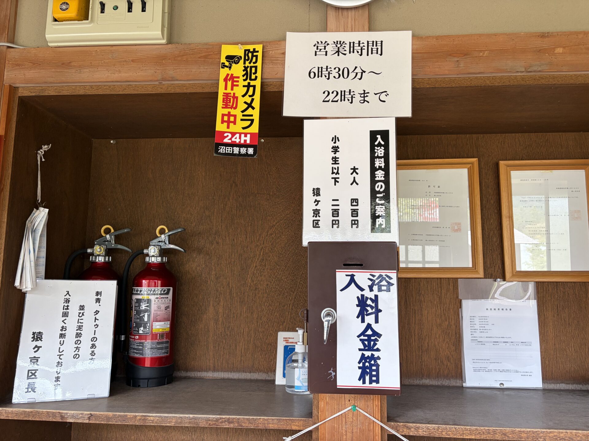 受付の棚。営業時間と料金の掲示、木の入浴料金箱