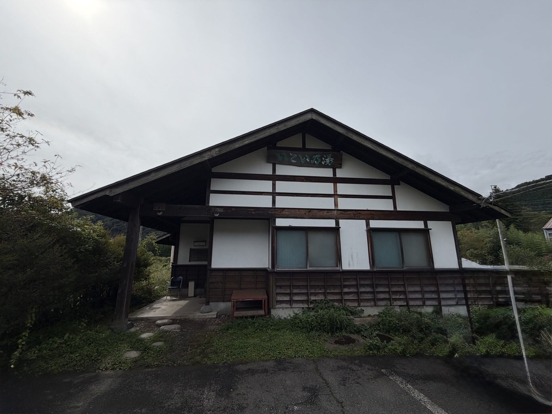 「いこい乃湯」の看板を掲げた木造平屋。軒下にパイプ椅子が1脚