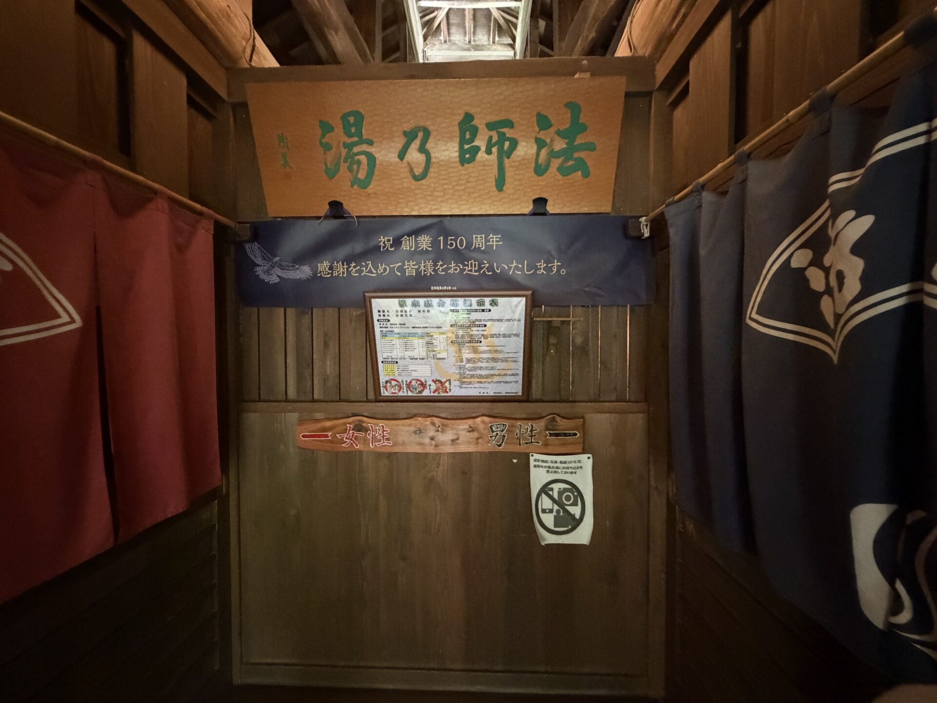 法師乃湯の入口。暖簾の脇に、撮影機器の浴室持ち込みを禁止する掲示