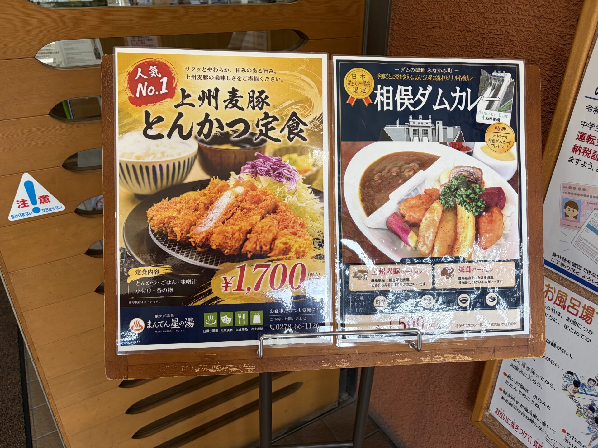 玄関のイーゼル。「人気No.1 上州麦豚とんかつ定食 1,700円」と相俣ダムカレーのポスター。下に「お食事だけでも気軽に」の文字
