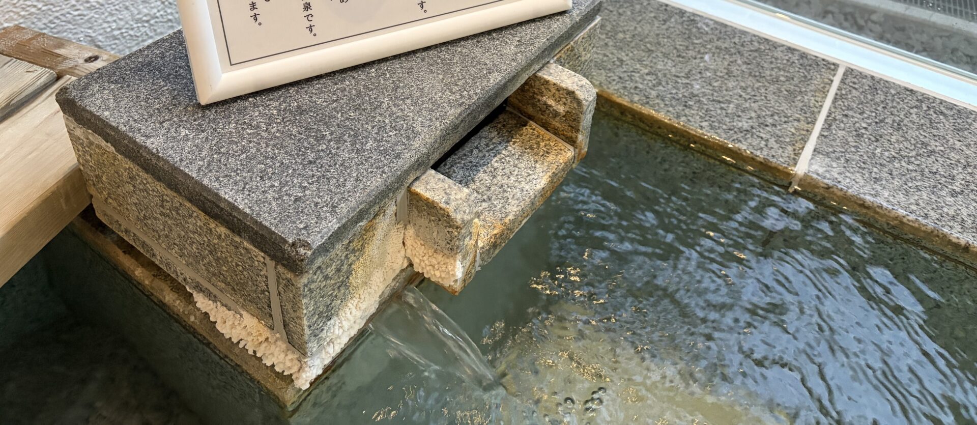 川原湯温泉 笹湯 内湯の湯口。石の下端に白い析出が固まって付き、熱い湯が浴槽に落ちている