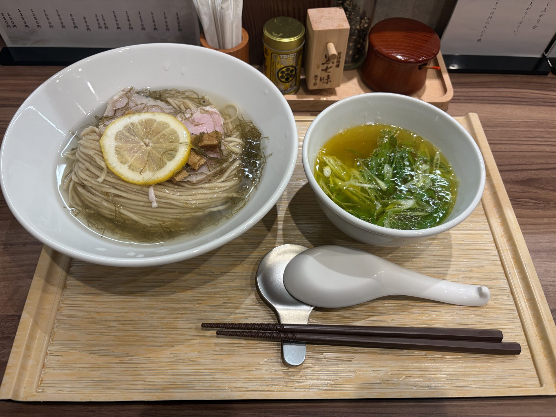 昆布水つけ麺（塩）。昆布水に浸った麺にレモンの輪切り、豚と鶏のチャーシュー、メンマ。隣にネギの入った塩のつけ汁
