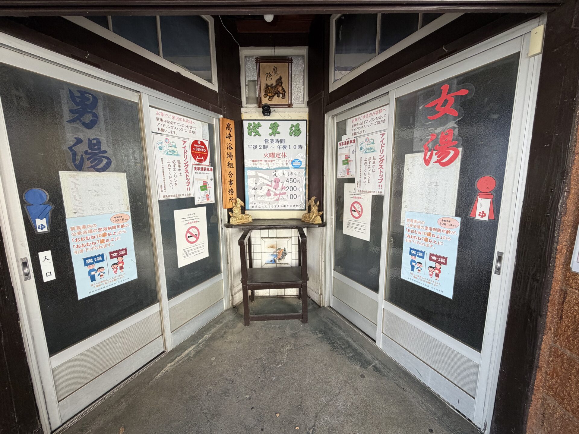 入口。左が男湯、右が女湯の引き戸。正面に営業時間と料金の札、上に「魔除」の額