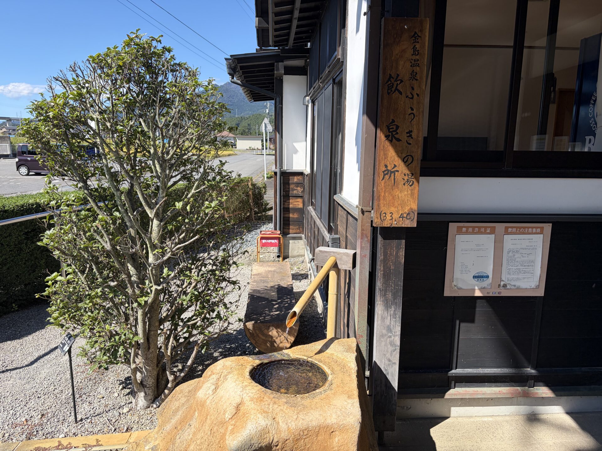 玄関脇の飲泉所。「金島温泉 ふうきの湯 飲泉所(33.4℃)」の木札と、石の鉢に湯を落とす注ぎ口