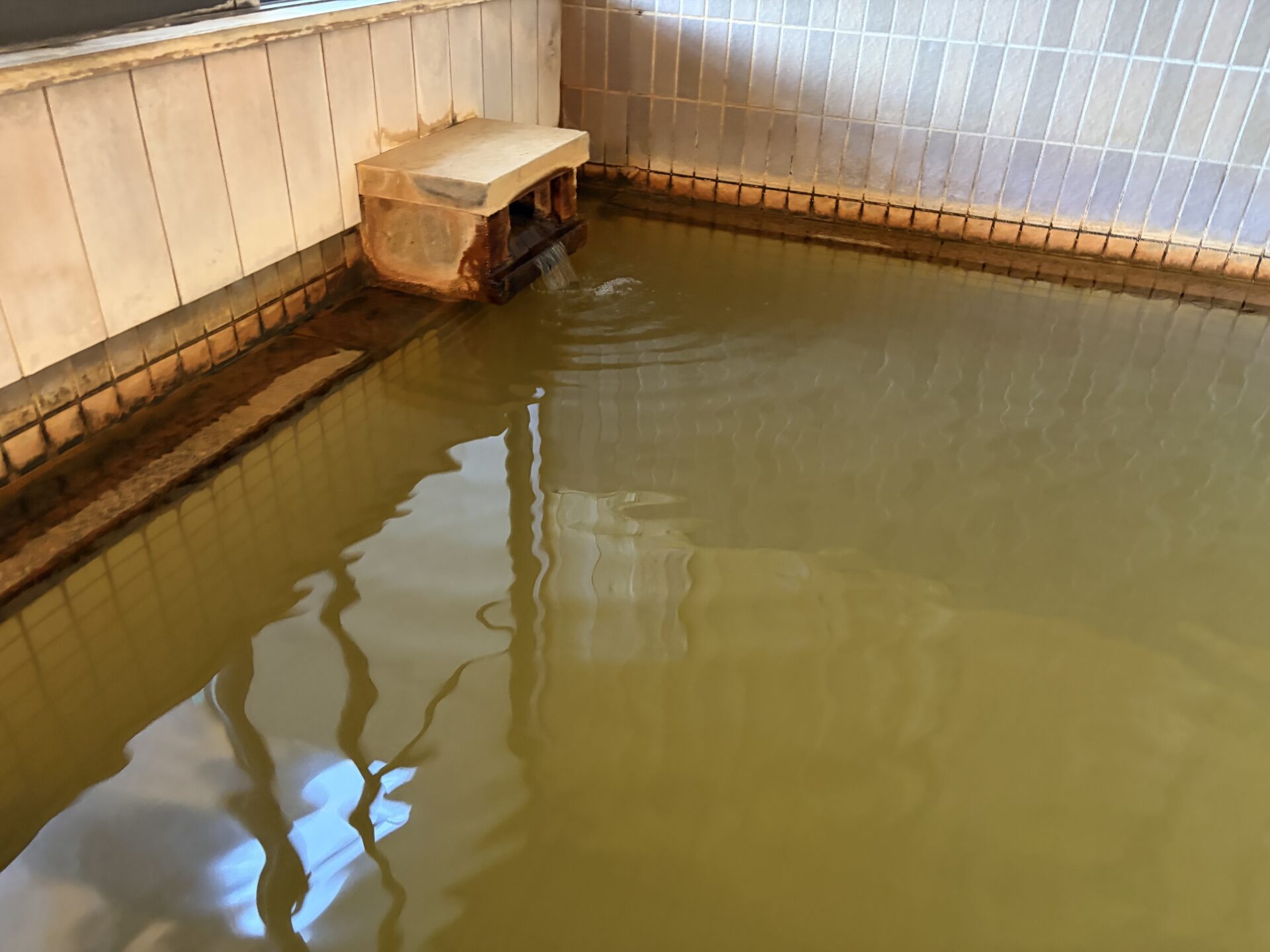 内湯の湯口。湯は黄土色で、湯口と浴槽の縁が赤茶色になっている
