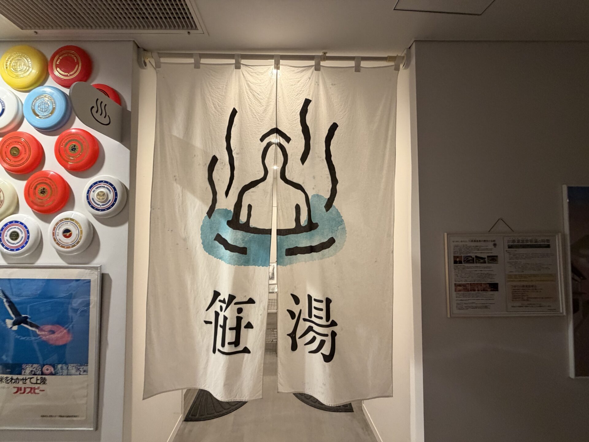 川原湯温泉 笹湯 温泉棟の暖簾「笹湯」。左の壁にはフリスビーが並んで展示されている