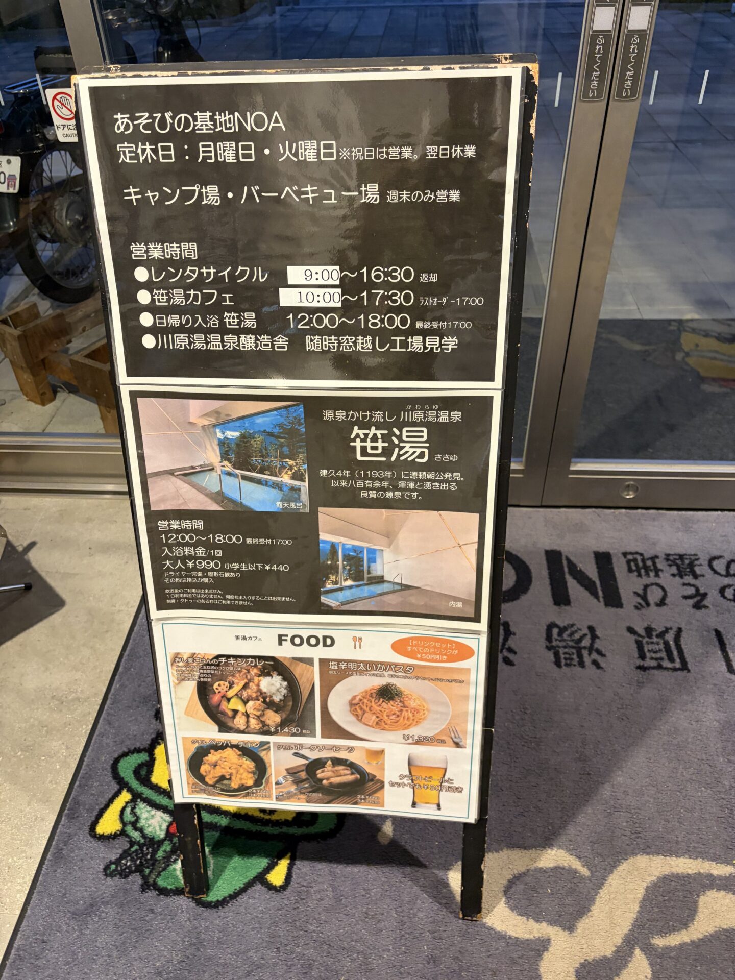 川原湯温泉 笹湯 入口の看板。定休日は月曜・火曜(祝日は営業し翌日休業)、日帰り入浴は12時から18時で最終受付17時、大人990円・小学生以下440円(看板の表記。ドア掲示は12歳以下)